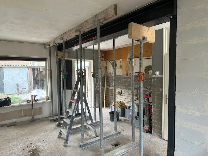 Draagmuur verwijderd in Tilburg 2 Doorbraak in woning in Tilburg waar een draagmuur is verwijderd, met een stalen draagbalk in het plafond en een trapladder op de bouwplaats
